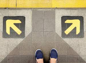 分かれ道に立ち、左右どちらに進むかを考えている足元の写真。選択と迷いを象徴する風